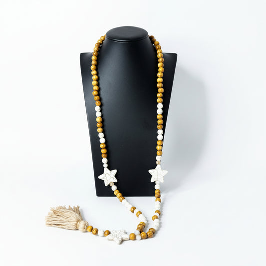 Necklace with star-shaped beads and a tassel on a black stand against a gray background