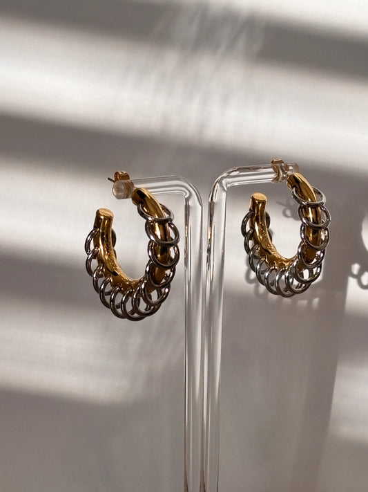 A pair of stainless steel chain tassel hoop earrings with double tones displayed on an ear stand.
