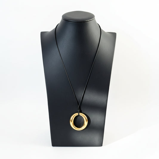 Audrey black cord necklace with an adjustable slider and polished gold pendant displayed on a mannequin neck stand, with decorative items in the background.
