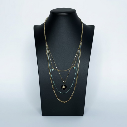 A gold-toned stainless steel necklace with turquoise accents displayed on a black mannequin, with decorative elements around it.