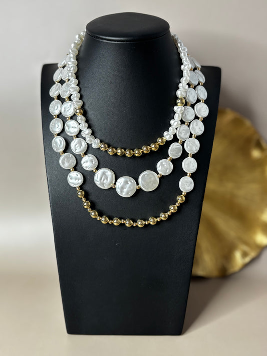 Multi-layered pearl and gold bead necklace on a black mannequin bust.