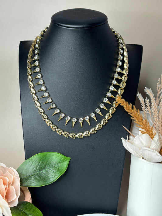 Gold Lavigne punk-style iron necklace with rhinestone inlays, displayed on a pedestal mannequin around decorative flowers.